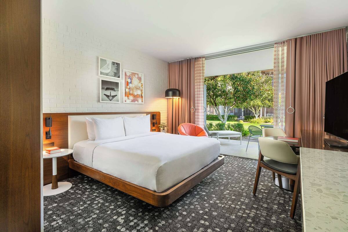 A hotel room with a bed, a desk, a chair, a TV, and a window with curtains.