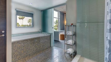 Een moderne badkamer met een groot bad, een raam met uitzicht op palmbomen, en een plank met handdoeken.