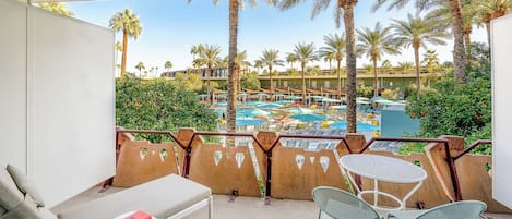 A balcony with a view of a pool area, lounge chairs, and a table with a book.