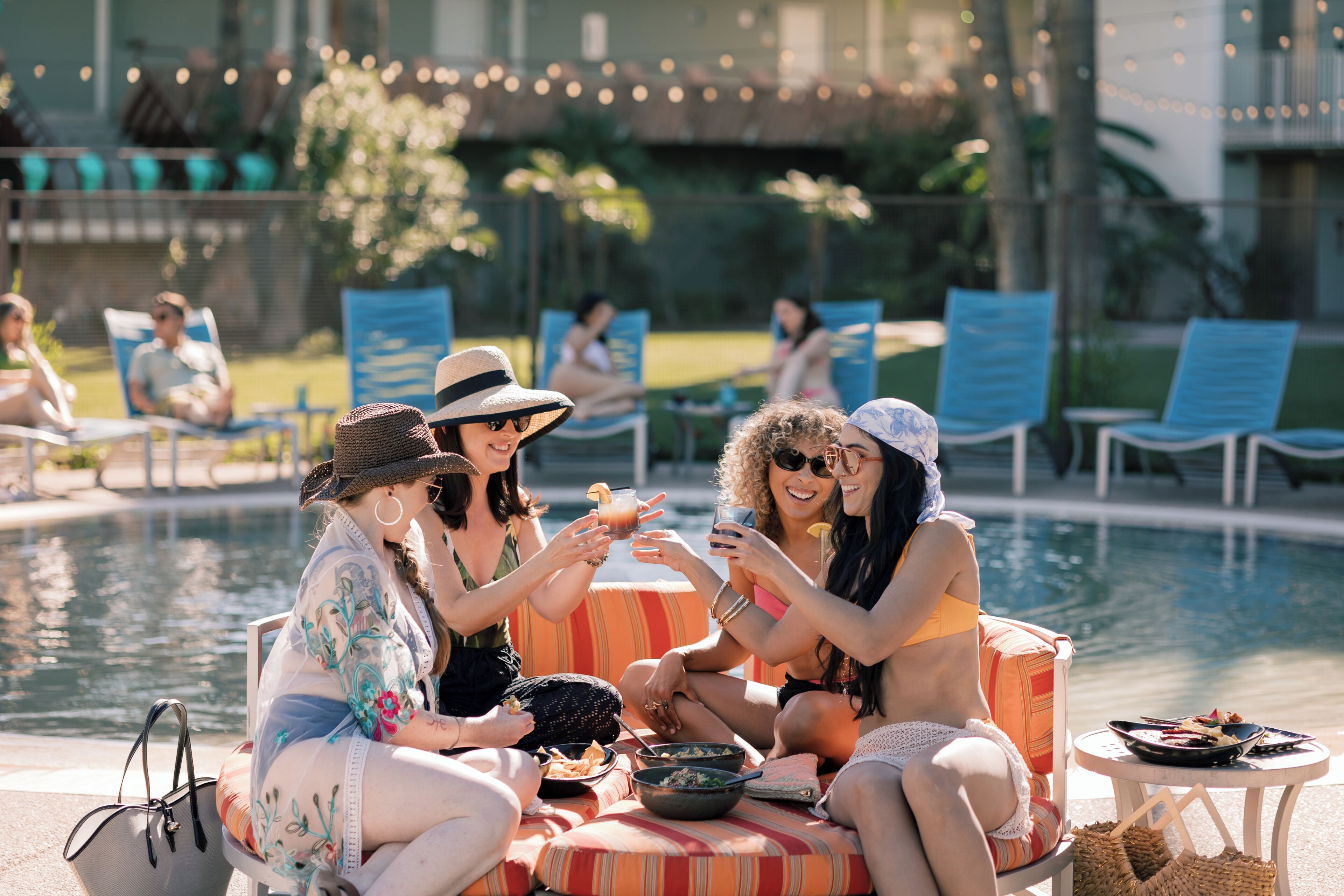 A poolside area with lounge chairs, a dining table, and a group of people socializing.