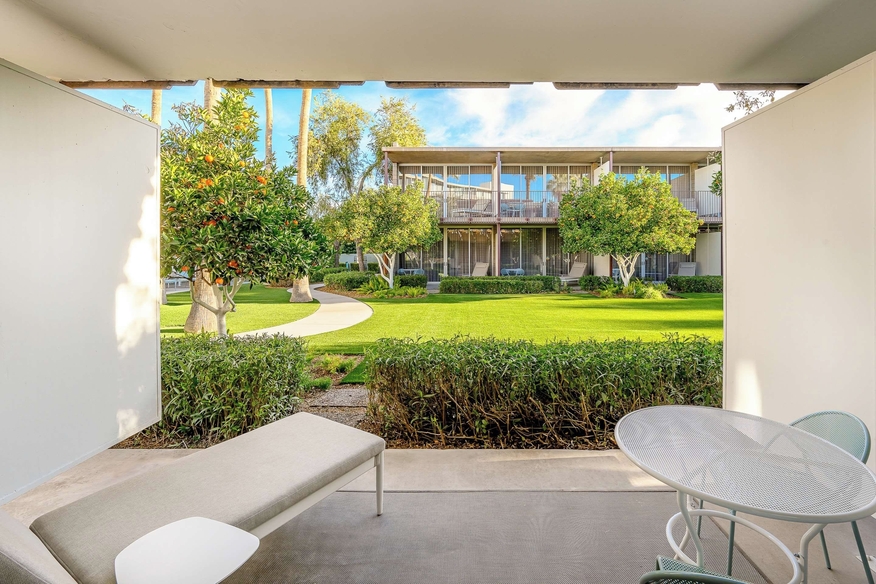 A modern outdoor patio with a seating area, a view of a well-maintained lawn, and a building with large windows and balconies.