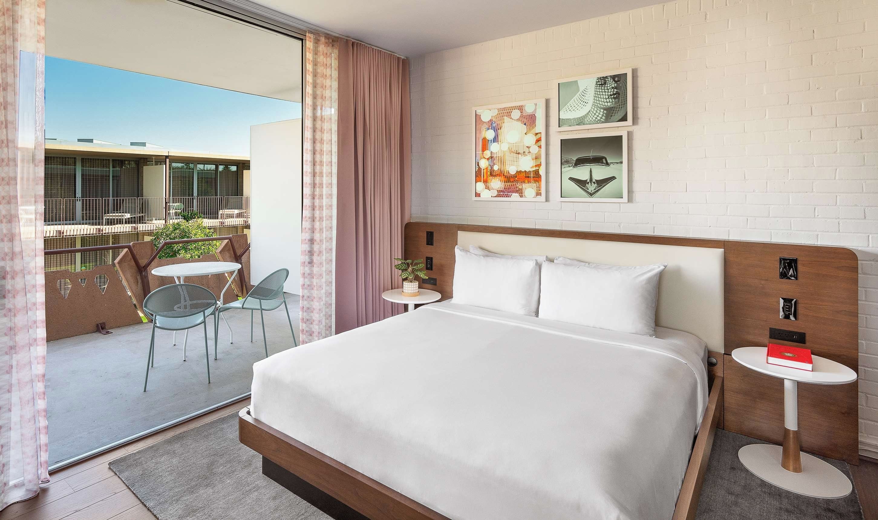 A hotel room with a large bed, a small table, a chair, and a balcony with a view.