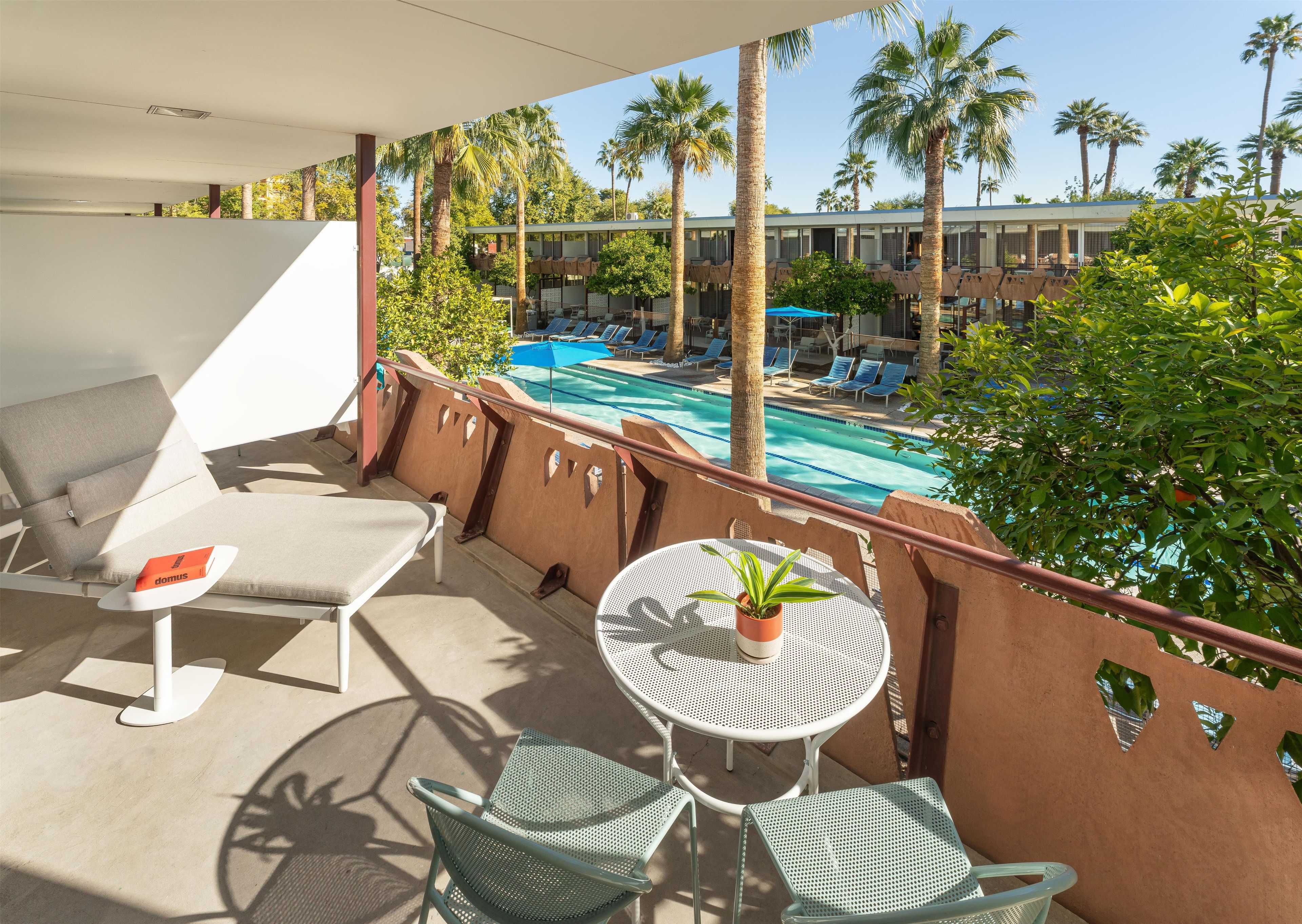 A balcony with a pool view, lounge chairs, and a table with a plant.