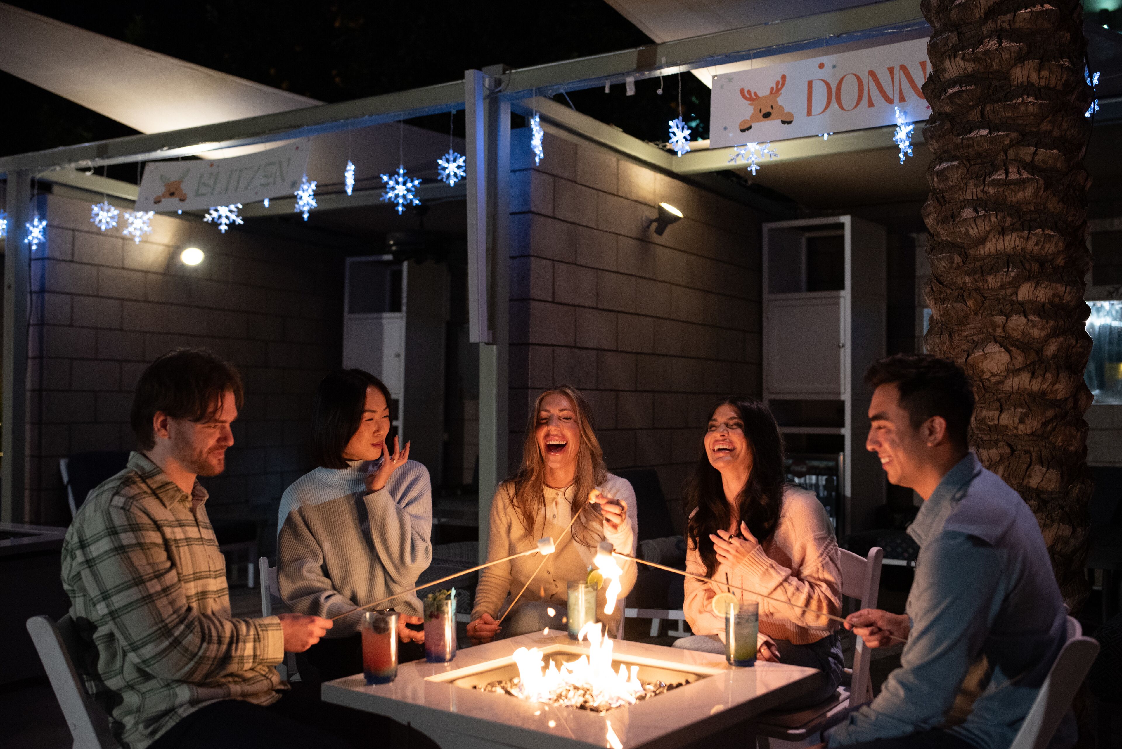 A group of people gathered around a fire pit with a sign above reading "DONN".