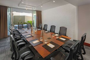Un salón de conferencias con una mesa larga, sillas negras y una pared de ladrillo blanco.