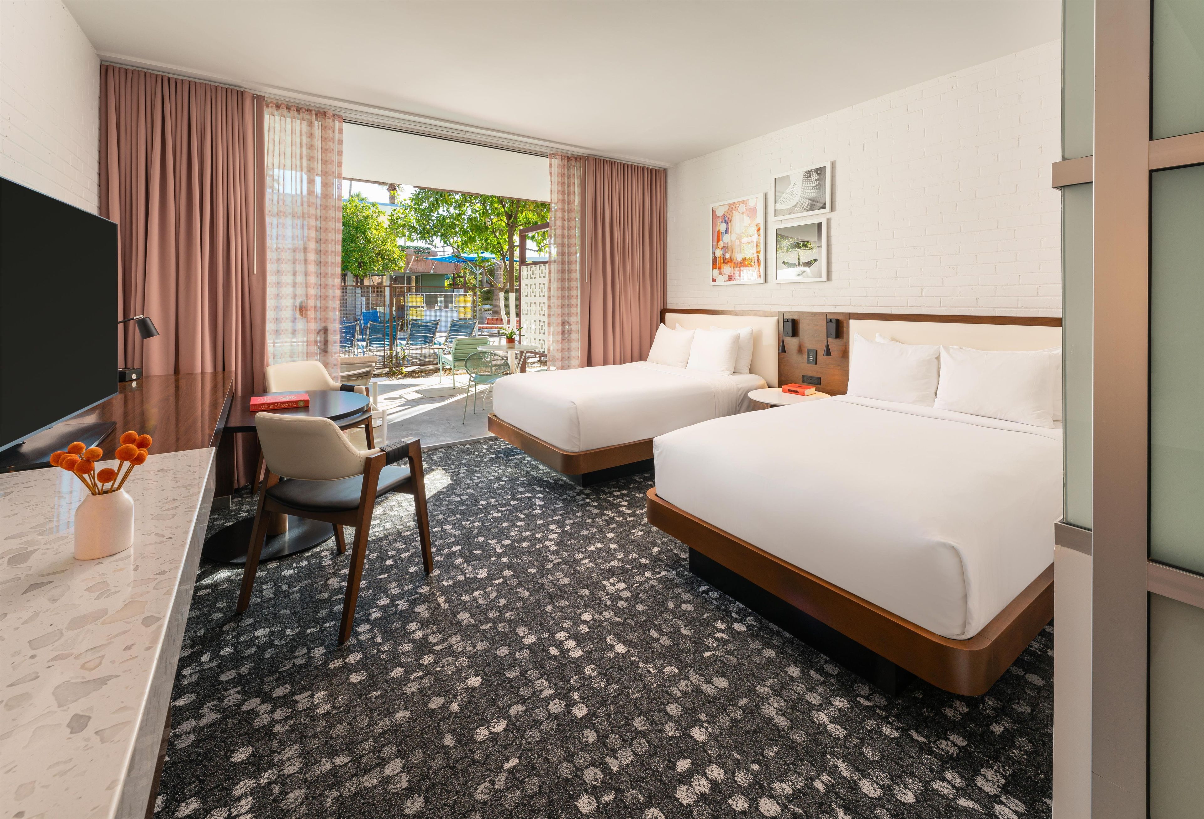 Habitación de hotel con dos camas, un escritorio con silla, televisión y vistas al área exterior.