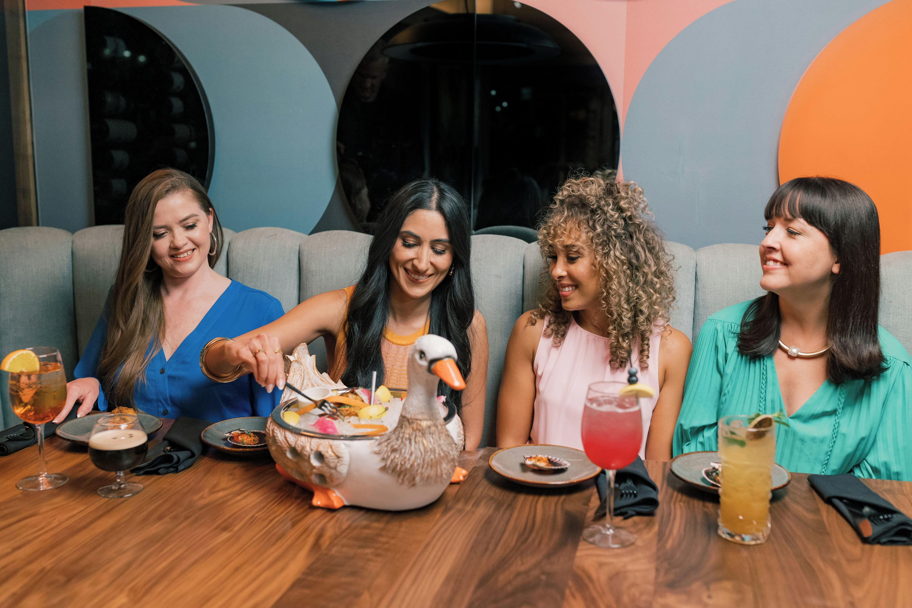 A group of people seated at a table with a decorative centerpiece, plates of food, and drinks.