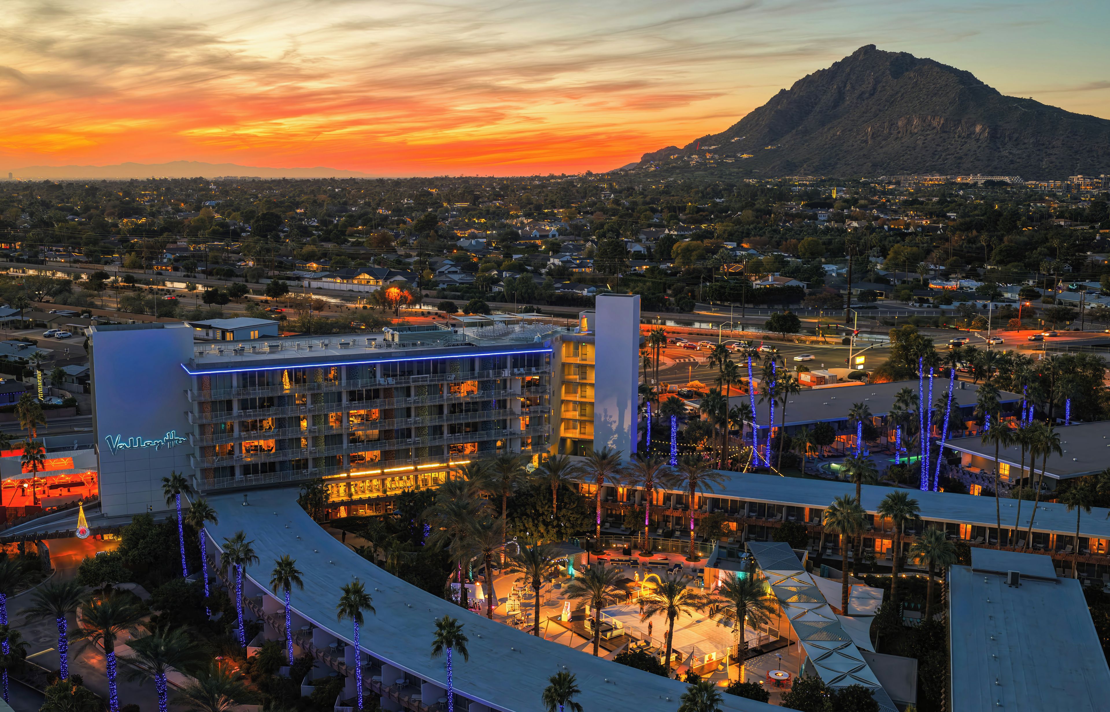 A hotel with multiple floors, a rooftop pool, and a view of a mountain.