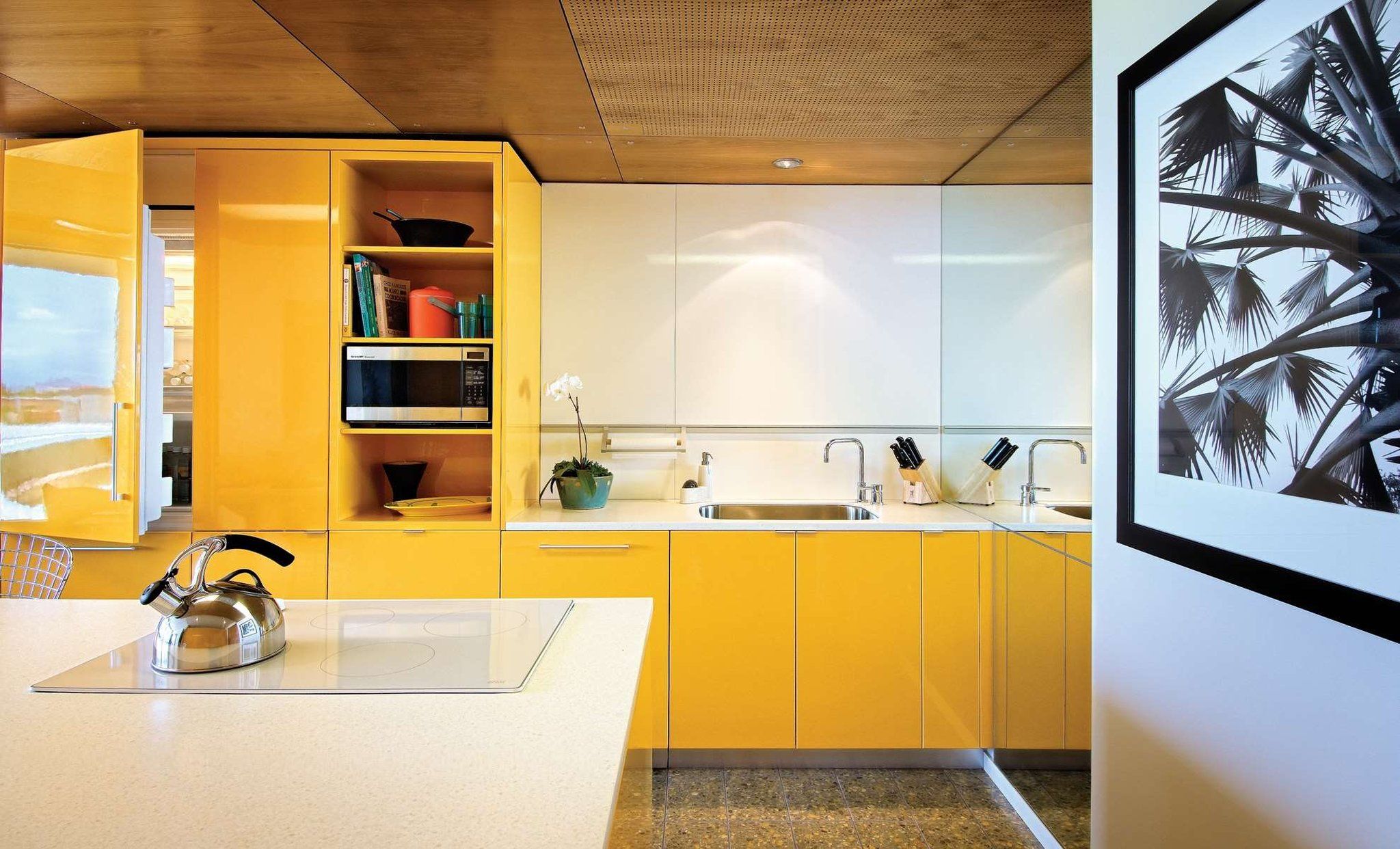 A modern kitchen with yellow cabinets, a stainless steel kettle, and a microwave.