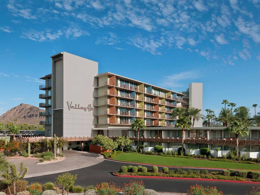 A multi-story hotel with a prominent 'Valley' sign, featuring balconies and a landscaped front yard with cacti and shrubs.