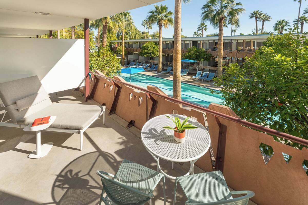 A balcony with a pool view, lounge chairs, and a table with a potted plant.