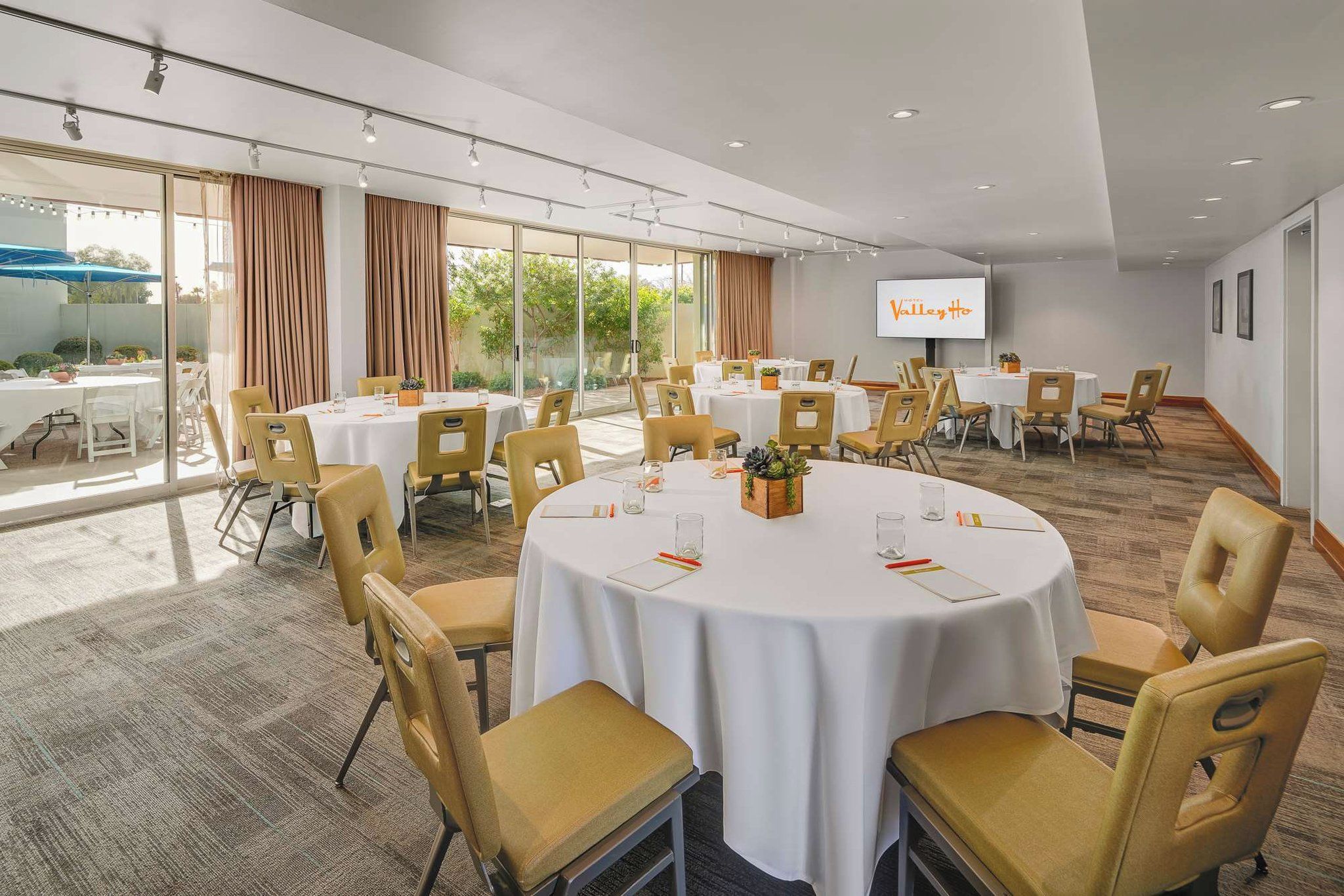 A conference room with round tables, chairs, and a large screen.