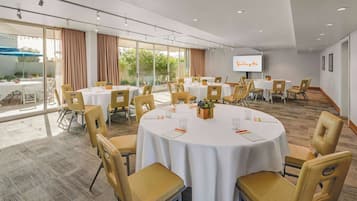 Sala de conferências com mesas redondas, cadeiras e uma tela grande.