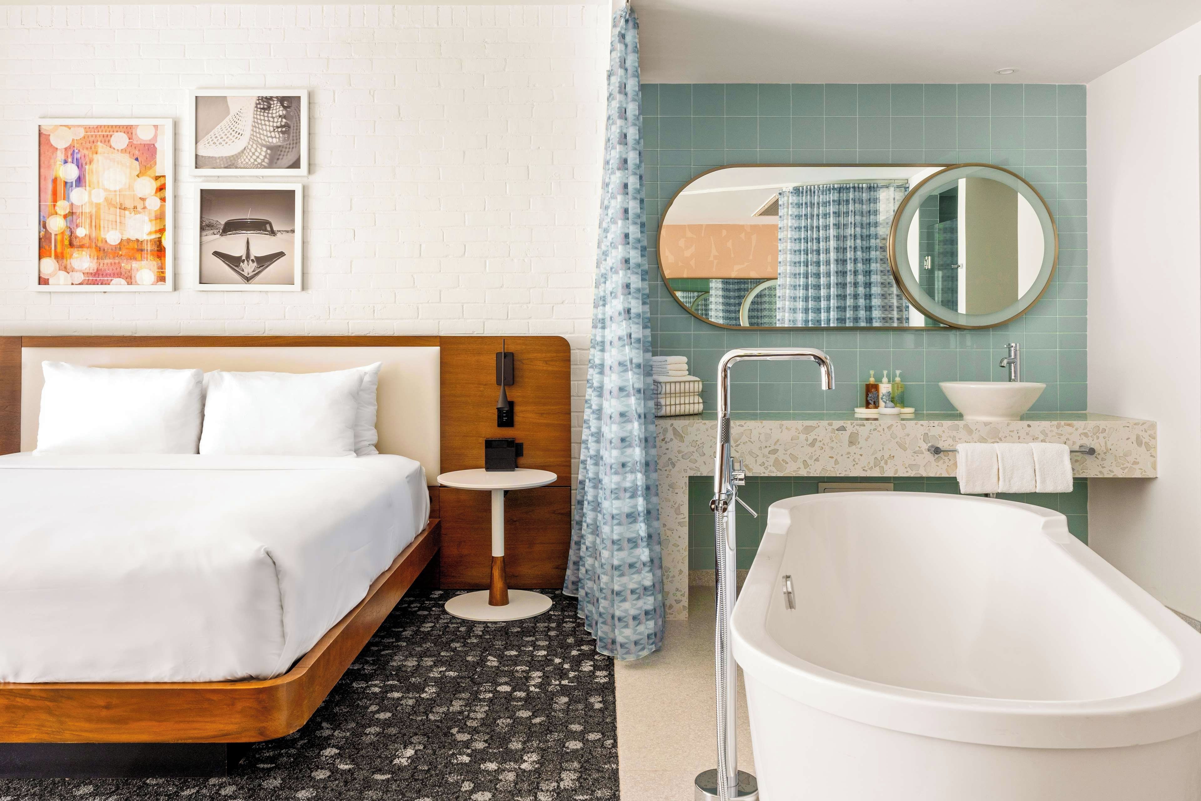 A hotel room with a bed, a round table, a bathroom with a bathtub, a sink, and a mirror.