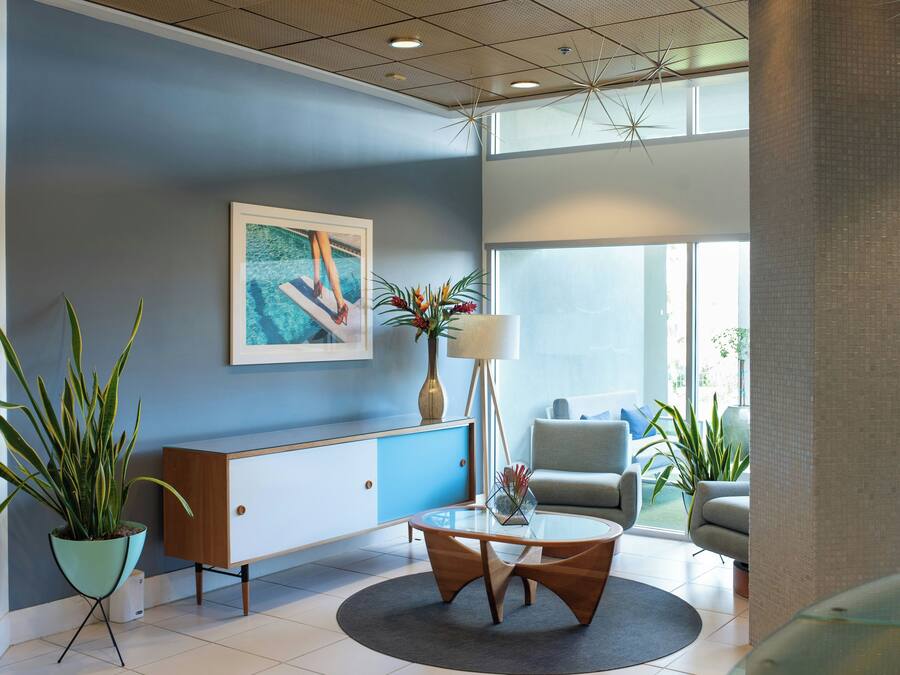 Un vestíbulo moderno con pared azul, un cuadro enmarcado, una planta en maceta, una mesa de centro redonda y una zona de estar con sofá y sillones.
