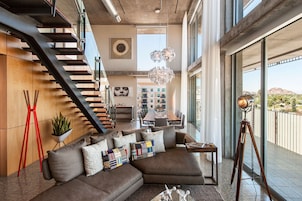 A modern living room with a large sectional sofa, a staircase, a dining area, and a balcony with a view.