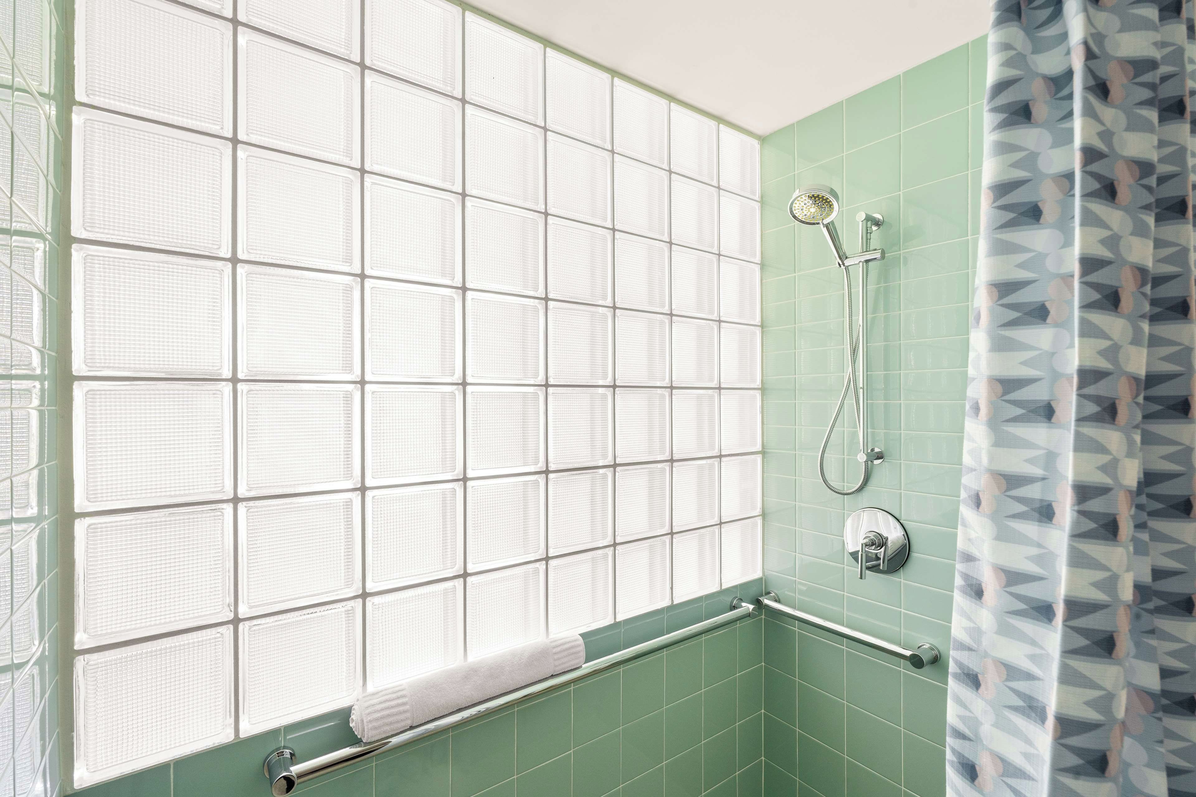 A bathroom with a shower, a towel rack, and a window with frosted glass panels.