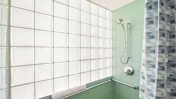 A bathroom with a shower, a towel rack, and a window with frosted glass panels.