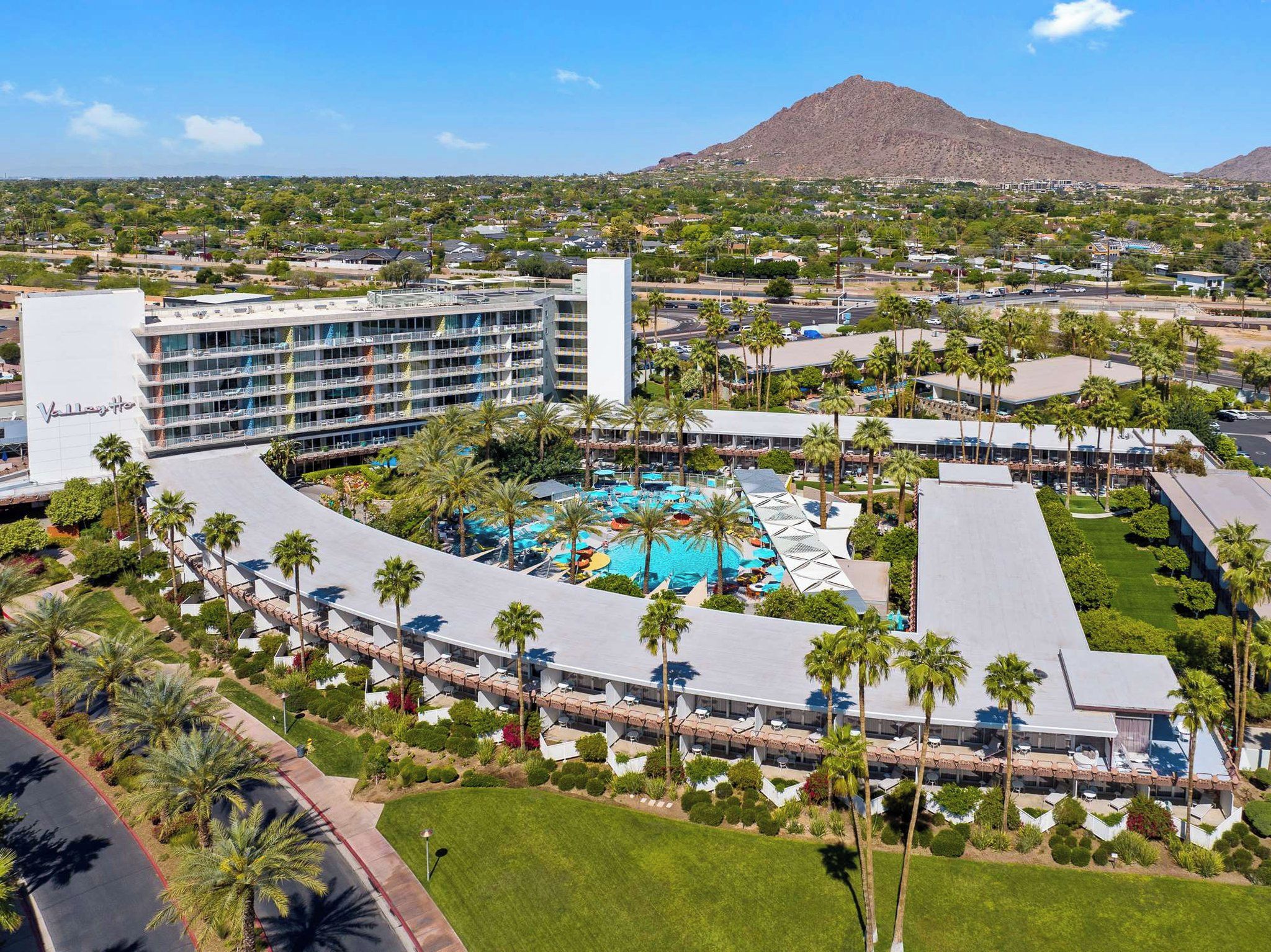A hotel with a central pool surrounded by palm trees and a mountain in the background.