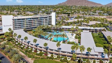 A hotel with a central pool surrounded by palm trees and a mountain in the background.