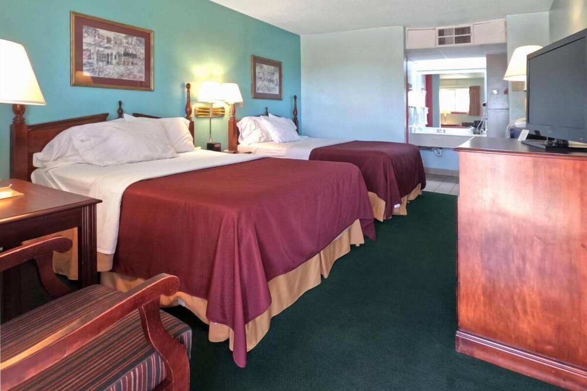 A hotel room with two beds, a desk, a chair, a television, and framed pictures on the wall.