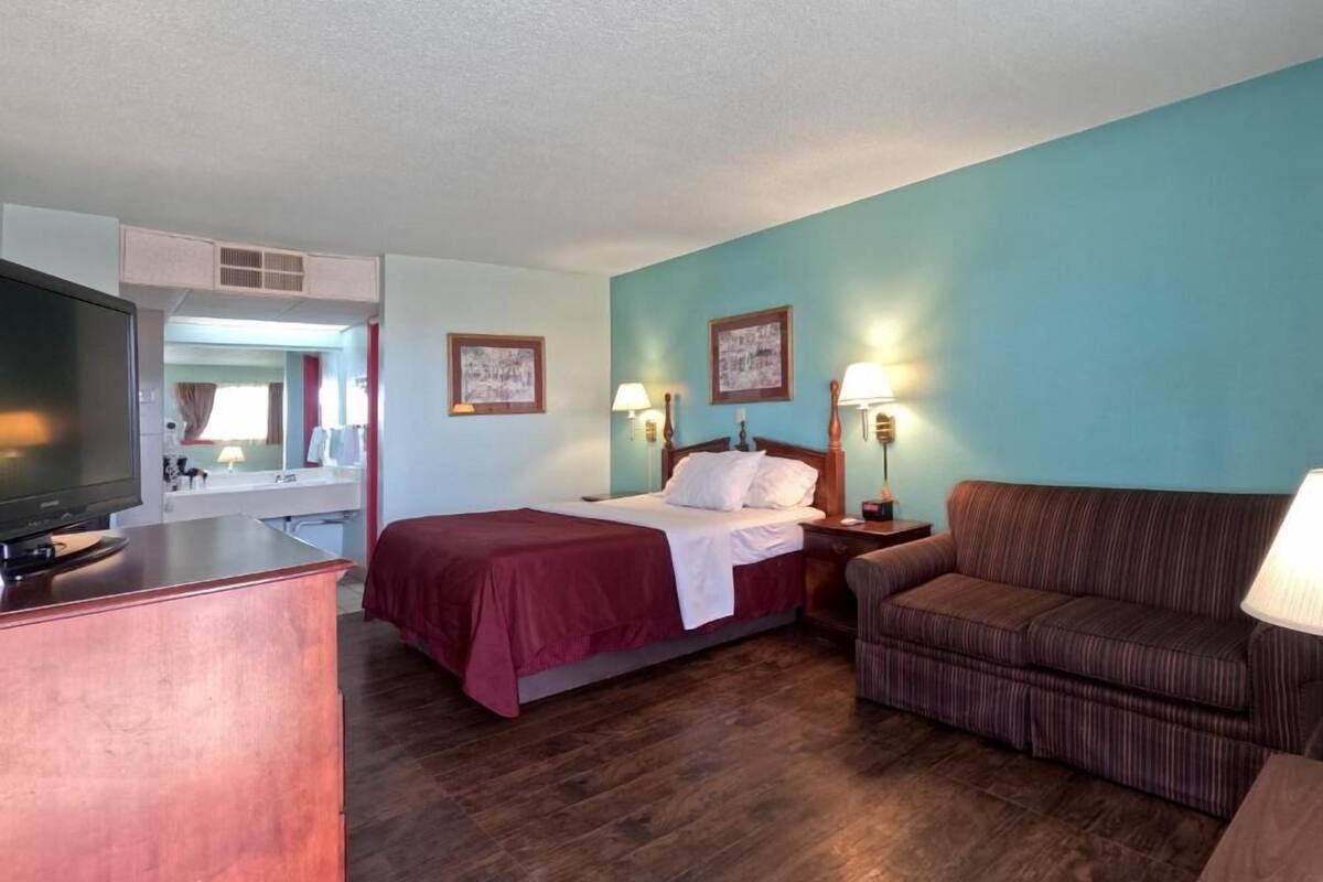 A hotel room with a bed, a sofa, a desk with a television, and two wall-mounted lamps.