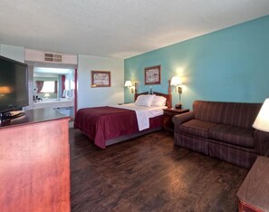 A hotel room with a bed, a sofa, a desk with a television, and two wall-mounted lamps.