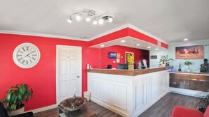 Ein modernes Wohnzimmer mit roter Akzentwand, einem weißen Empfangstisch und einer großen Uhr.