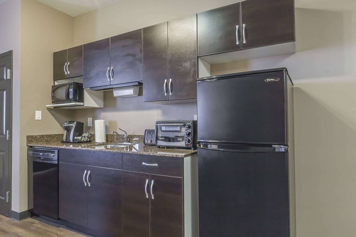 A modern kitchen with dark cabinets, a microwave, a toaster, and a refrigerator.