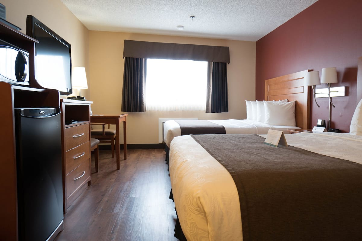 A hotel room with two beds, a desk, a chair, a TV, and a window with curtains.
