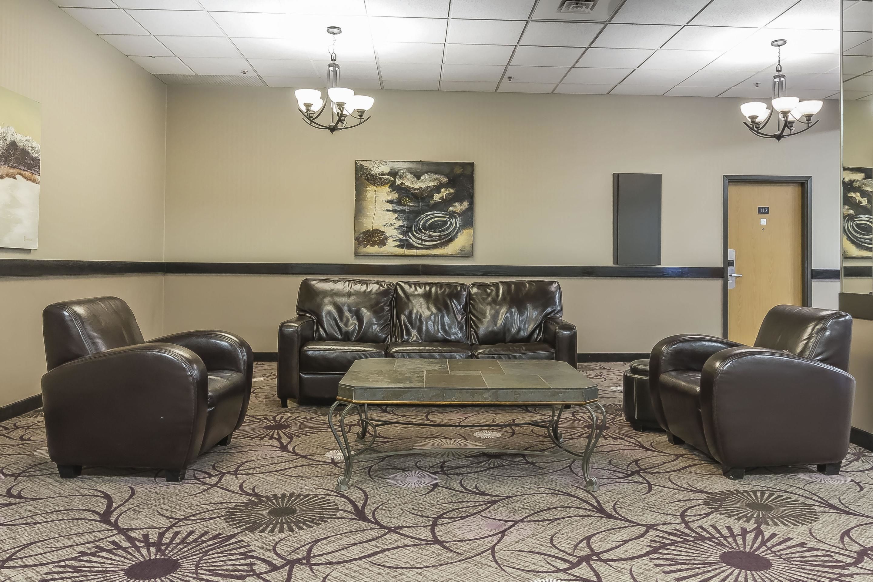 A lobby with leather sofas, a metal coffee table, and a chandelier.