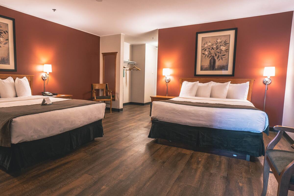 A hotel room with two beds, wooden flooring, and framed artwork on the walls.