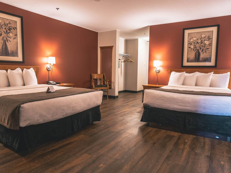 A hotel room with two beds, wooden flooring, and framed artwork on the walls.
