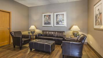 A lobby with a leather sofa, two armchairs, a matching ottoman, and two lamps on side tables. There are framed artworks on the wall and a wooden door on the left.