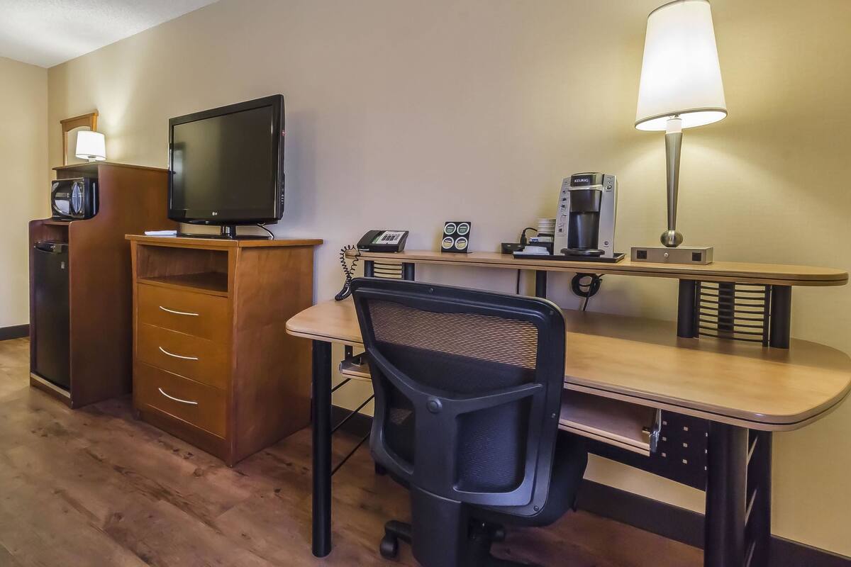 A hotel room with a wooden desk, a black office chair, a television, a coffee maker, a telephone, and a microwave.