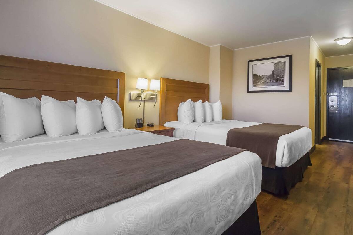 A hotel room with two beds, a nightstand with a lamp, a framed picture on the wall, and a door leading to the bathroom.