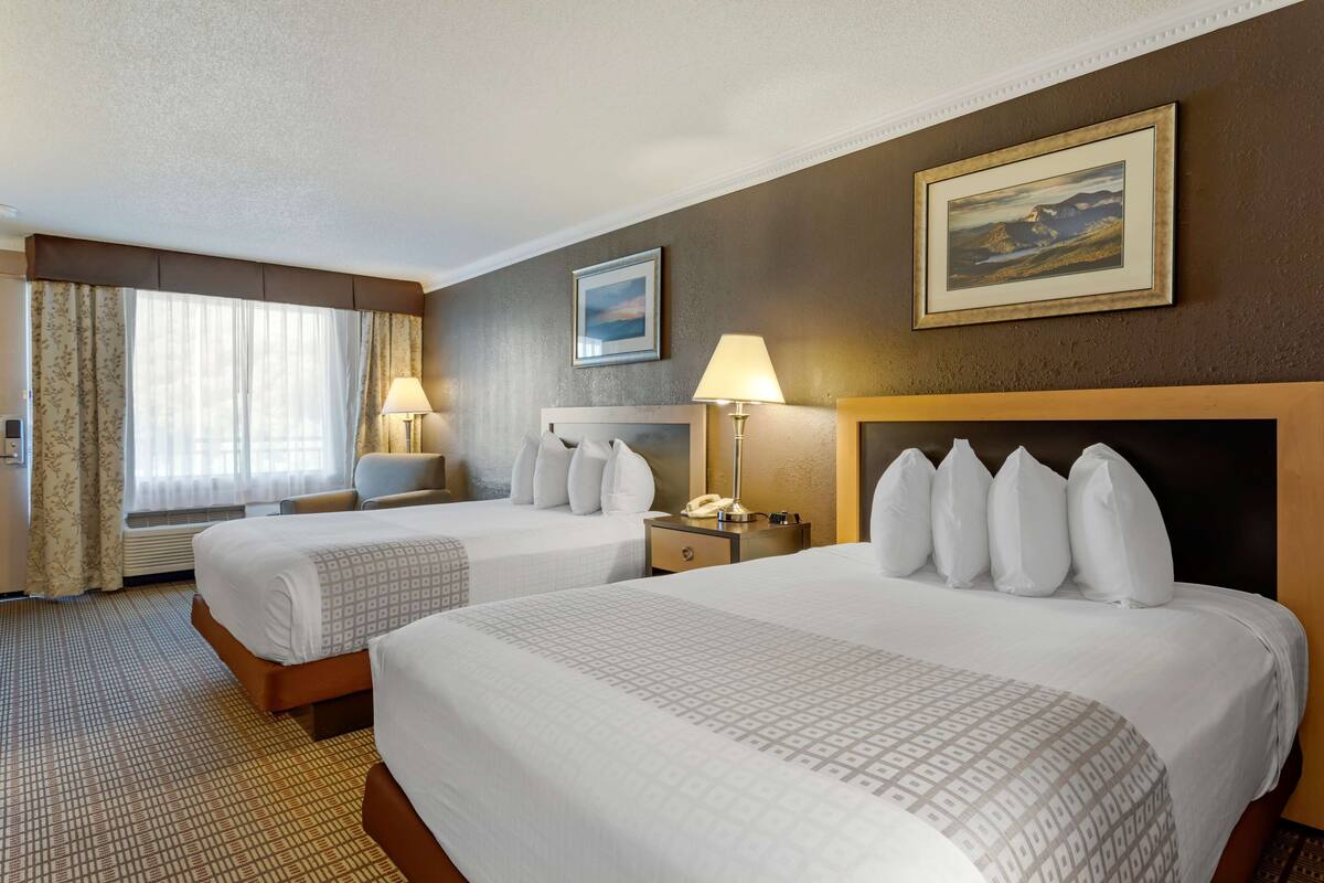 A hotel room with two beds, a desk, a chair, a lamp, and a painting on the wall.