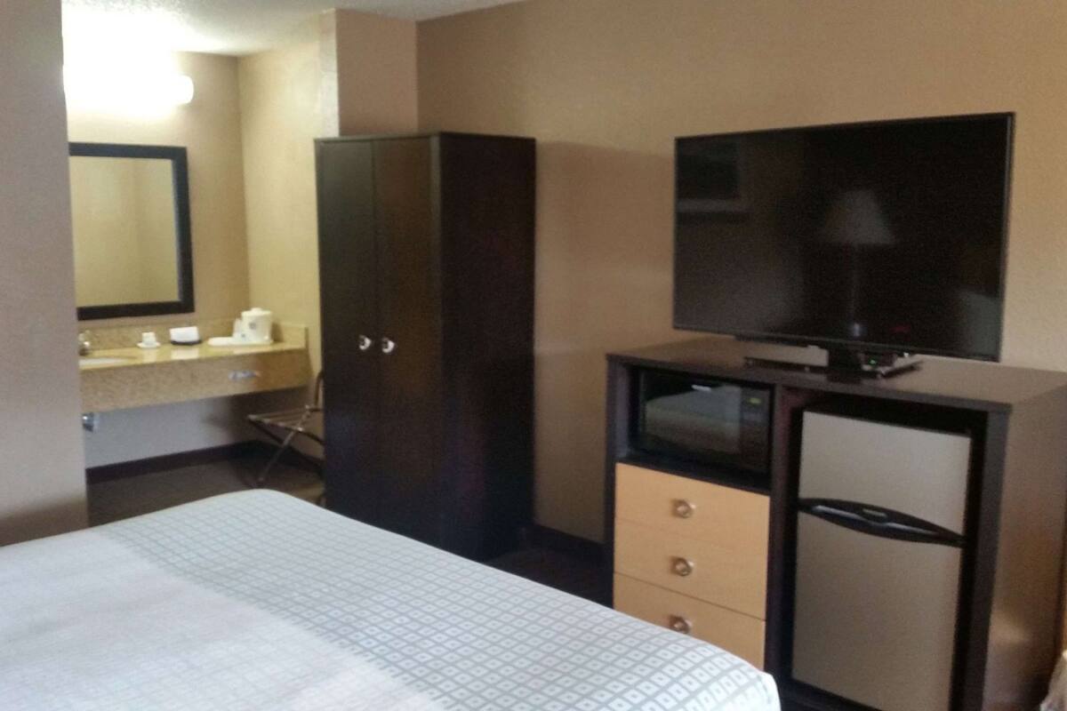 A hotel room with a bed, a TV on a stand, a wardrobe, and a bathroom with a sink and mirror.
