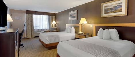 Quarto de hotel com duas camas, uma escrivaninha, uma cadeira, um abajur, um telefone e um quadro na parede.