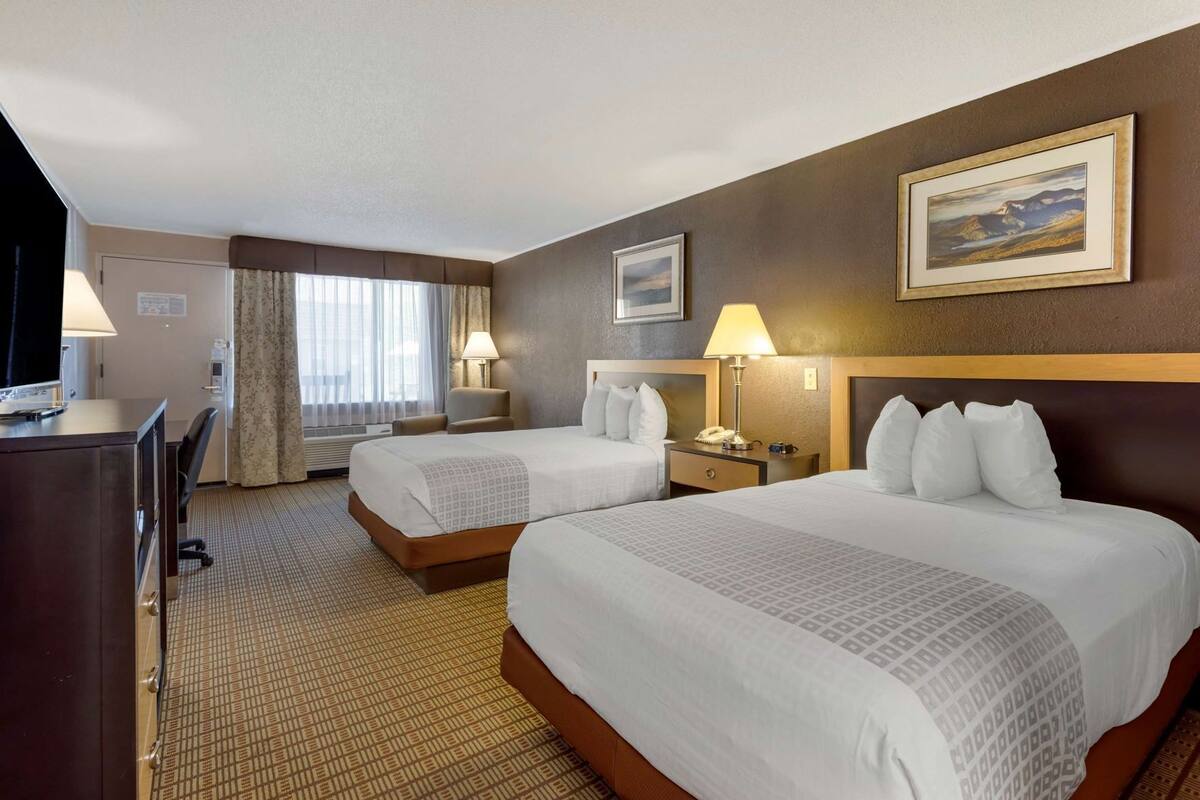 A hotel room with two beds, a desk, a chair, a lamp, and a painting on the wall.