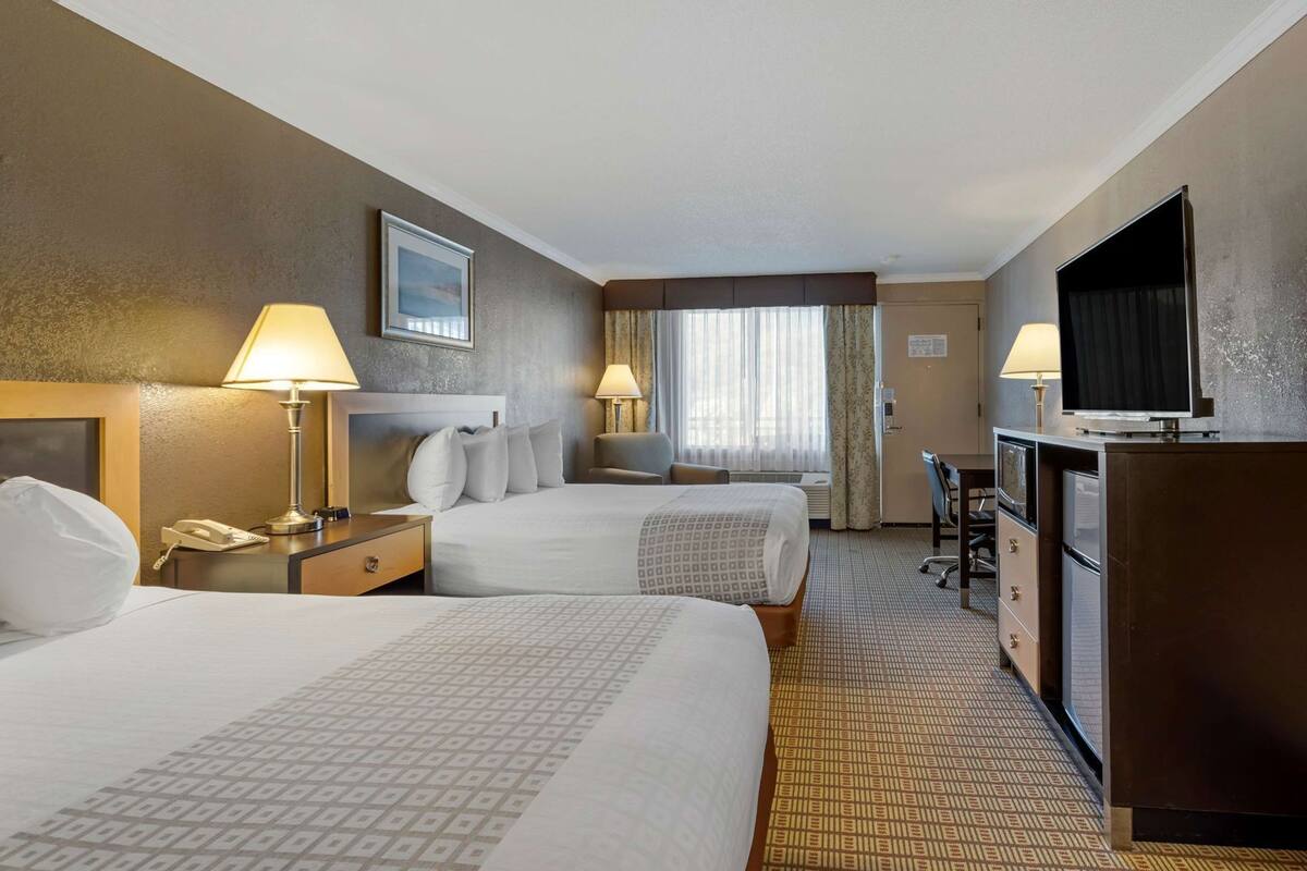 A hotel room with two beds, a desk, a television, and a window with curtains.
