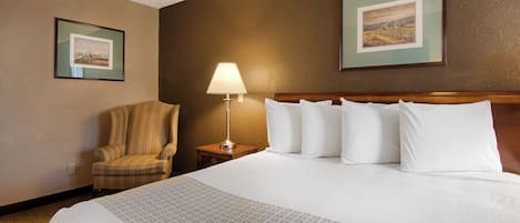 A hotel room with a large bed, a chair, a nightstand with a lamp, and two framed pictures on the wall.