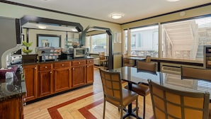 A modern kitchen with wooden cabinets, a central island, and a dining area with a glass table and chairs. - Best Western Smoky Mountain Inn (Waynesville)