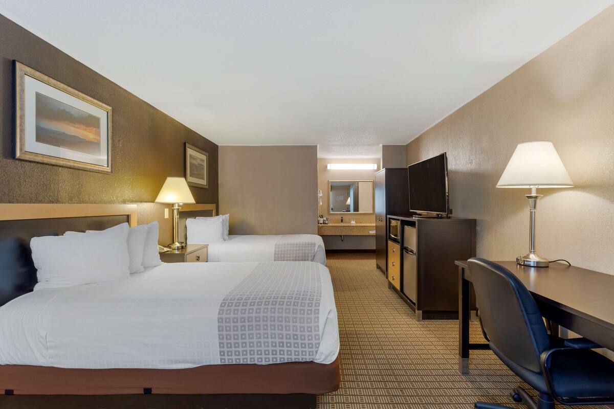 A hotel room with two beds, a desk, a TV, and a bathroom with a mirror and sink.