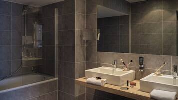 A modern bathroom with a glass-enclosed shower, two sinks, and a vanity with toiletries.
