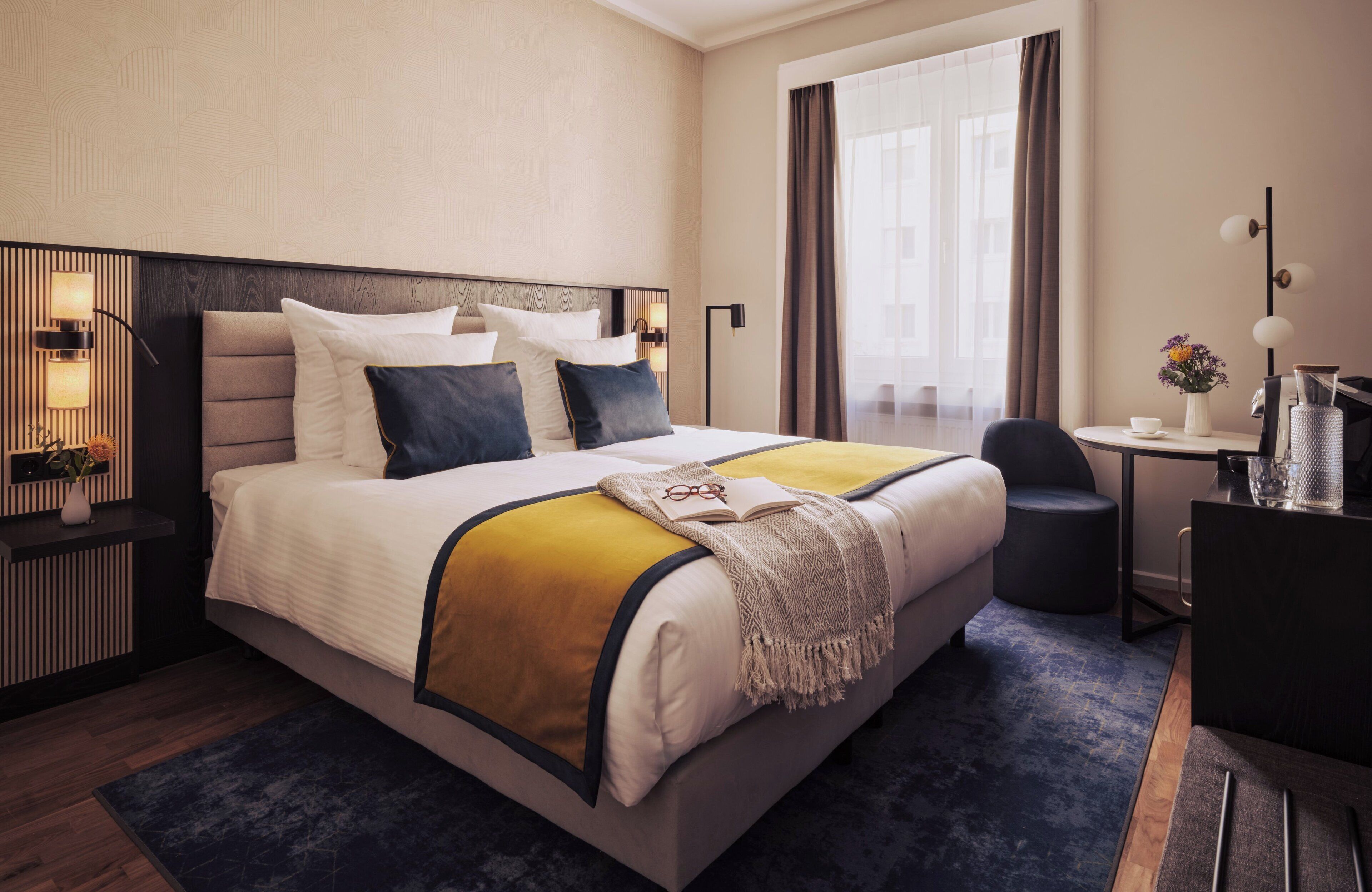 Quarto de hotel moderno com uma cama grande, mesas de cabeceira, uma escrivaninha e vista para o exterior.