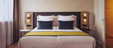A double bed with a headboard, two bedside tables with lamps, a bedside table with a vase, and a door to the right.