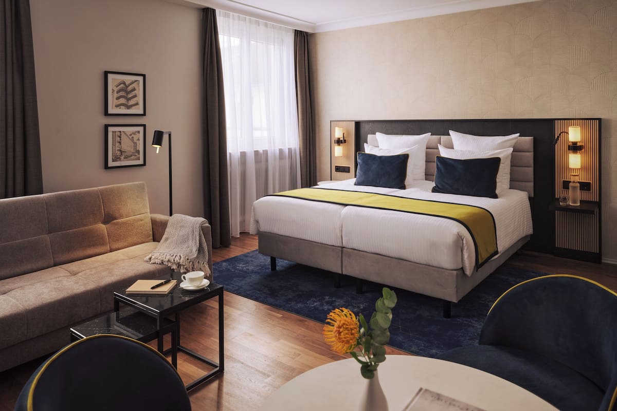 Quarto de hotel com cama, sofá, mesa pequena e cadeira.