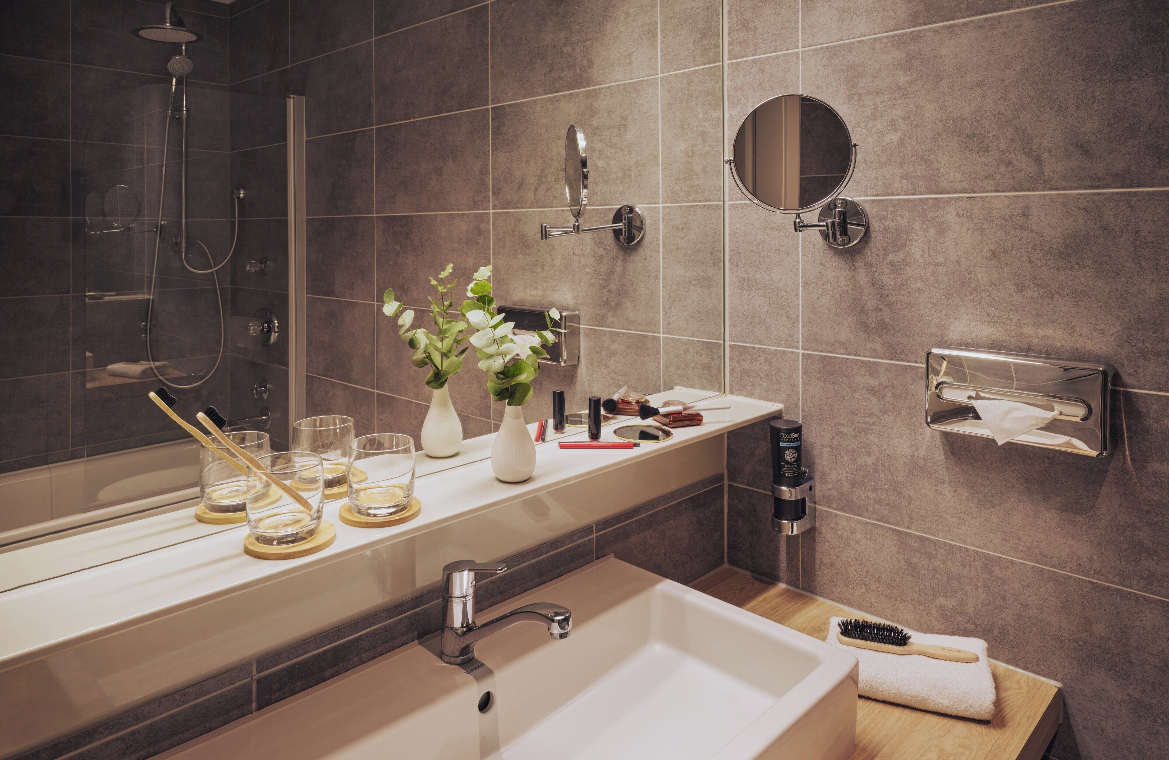 A modern bathroom with a large mirror, a sink, a shower, and a towel rack.