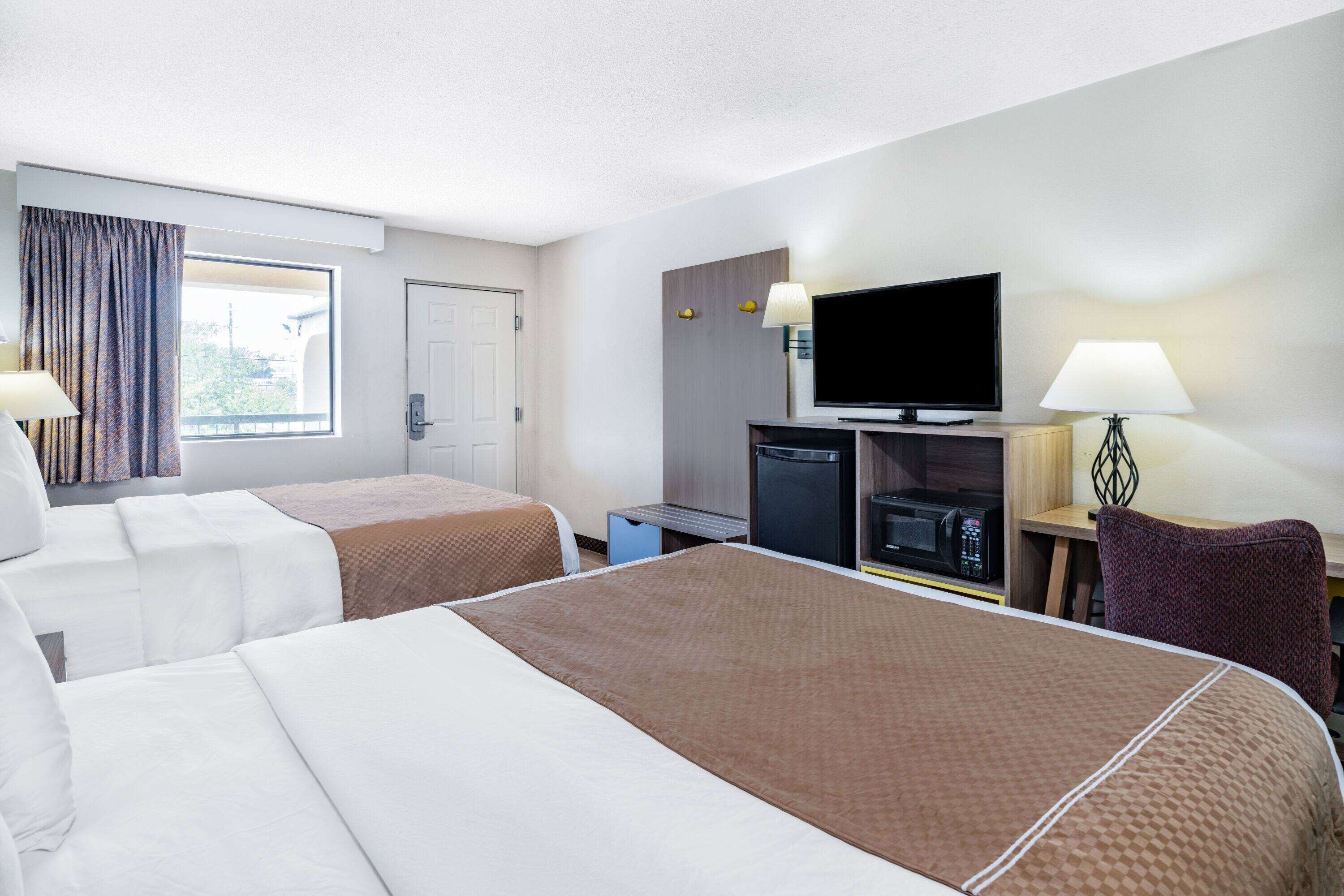 A hotel room with two beds, a television, a microwave, and a desk with a chair.